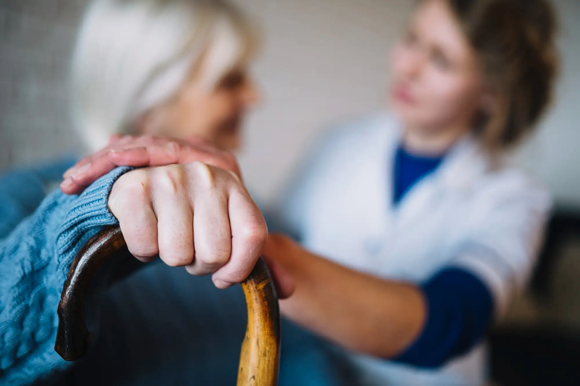Person und Oma leicht verschwommen im Hintergrund, der Fokus liegt auf den Händen der beiden, die Person hat die Hand auf der Hand der Oma